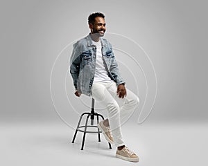Handsome young african american guy sitting on stool, posing in studio - isolated