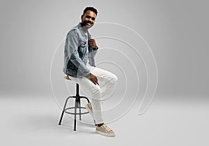 Handsome young african american guy sitting on stool, posing in studio - isolated