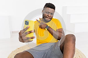 Handsome young African American male in yellow sportswear sitting on floor at home and embracing knee while smiling and