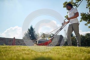 Handsome young african american man mowing grass outdoors, making the backyard beutiful and neat