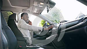 Handsome young african american man sitting on the front leather seat black luxury car and tunes the vehicle touch