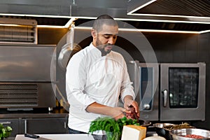 Handsome young African chef standing in professional kitchen in restaurant preparing a meal of meat and cheese vegetables