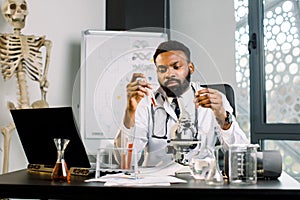 Handsome young African male scientist biologist virologist studying reaction of some chemical substance, new vaccine or
