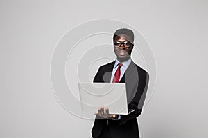 Handsome young African man in formalwear working on laptop while standing against grey background