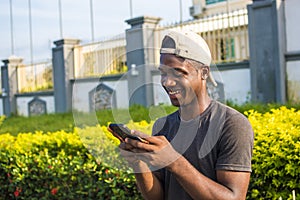 handsome young african man smiling and using his phone, browsing the internet, surfing the web