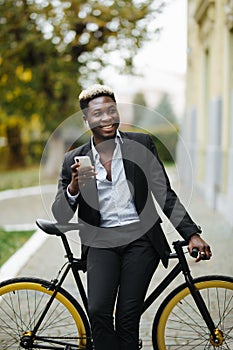 Handsome young african man standing with bicycle, listening to music with headphones in the street outdoors