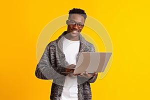 Handsome young african man using laptop on yellow