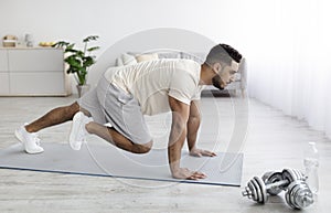 Handsome young Arab guy in sportswear exercising on yoga mat, doing domestic fitness, working out his muscles at home