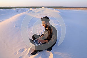 Handsome young Arab man writes on Internet using laptop and sits