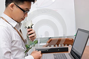 Handsome young Asian business man preparing a white rose for his girlfriend in valentines day. Love and romance in workplace conce
