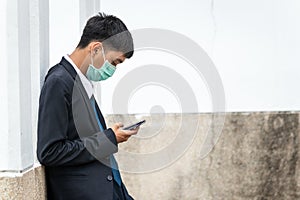 A handsome young asian business man using smartphone. Asian young attractive businessman wearing a face mask leaning against the