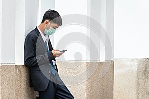 A handsome young asian business man using smartphone. Asian young attractive businessman wearing a face mask Stand against the