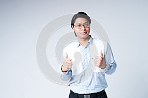 Handsome young Asian businessman in shirt wearing glasses and trousers throws thumbs up. Isolated on gray background