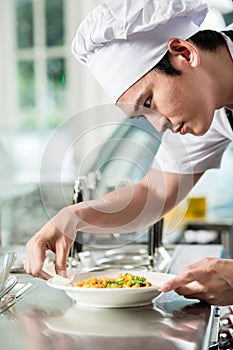 Handsome young Asian chef plating up food