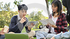 Handsome young Asian male college student using his tablet, with his friends in the campus`s park