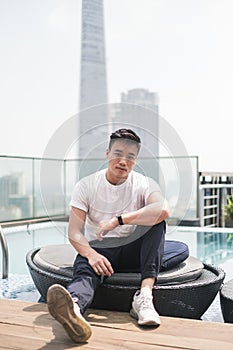 Handsome young Asian man sitting on the rooftop near the swimming pool