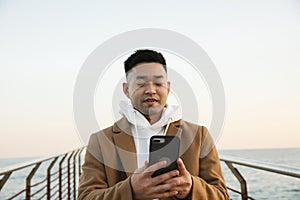 Handsome young Asian man using his smartphone on the beach. Freelance concept.