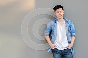Handsome young Asian man wear denim shirt, looking at camera. Portrait young Asia cool guy with hands in pockets leaning against