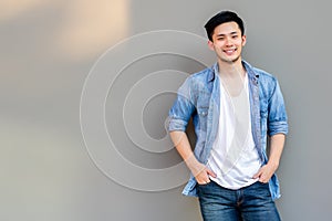 Handsome young Asian man wear denim shirt, looking at camera. Portrait young Asia cool guy with hands in pockets leaning against