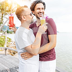 Handsome young attractive male couple, gay couple and family, Valentine`s Day at a tropical resort with cocktails in their hands