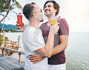 Handsome young attractive male couple, gay couple and family, Valentine`s Day at a tropical resort with cocktails in their hands