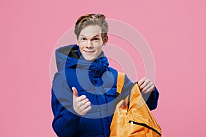 a handsome young attractive man with red hair stands in a dark-colored winter outerwear showing a thumbs up and holds a