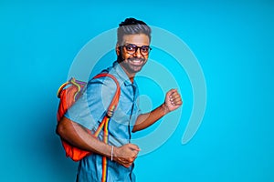 handsome young bearbed indian man with eye glasses in blue cotton t-shirt with orange rainbow backpack in studio