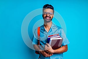 handsome young bearbed indian man with eye glasses in blue cotton t-shirt with orange rainbow backpack in studio