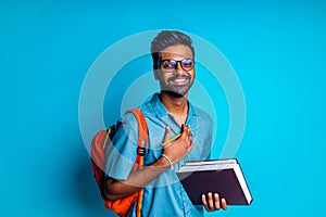 handsome young bearbed indian man with eye glasses in blue cotton t-shirt with orange rainbow backpack in studio