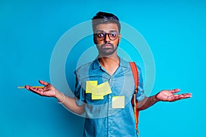 handsome young bearbed indian man with eye glasses in blue cotton t-shirt with orange rainbow backpack in studio