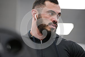 Handsome young bearded athlete man wearing black sportswear hoodie and wireless headphones during sport fitness workout training