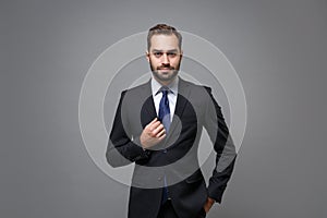 Handsome young bearded business man in classic black suit shirt tie posing isolated on grey background studio portrait