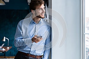 Handsome young bearded business man in office using mobile phone indoors.