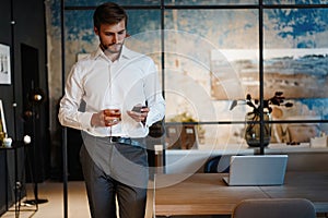 Handsome young bearded business man in office using mobile phone indoors.