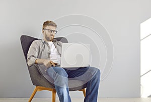 Handsome young bearded businessman sitting on chair in a empty space with laptop and working.