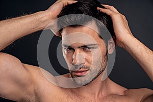 Handsome young bearded man isolated. Portrait of shirtless muscular man is standing on grey background and holding his hair