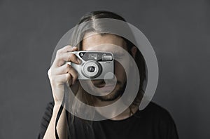 Handsome young bearded man with a long hair and in a black shirt holding vintage old-fashioned film camera on a black