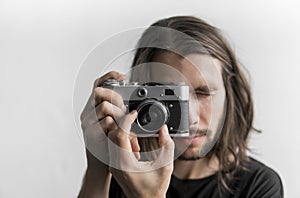 Handsome young bearded man with a long hair and in a black shirt holding vintage old-fashioned film camera on a white