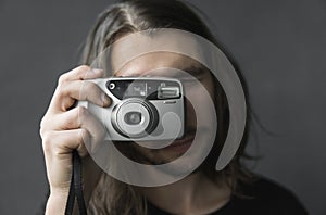 Handsome young bearded man with a long hair and in a black shirt holding vintage old-fashioned film camera on a black