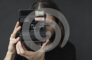 Handsome young bearded man with a long hair and in a black shirt holding vintage old-fashioned film camera on a black