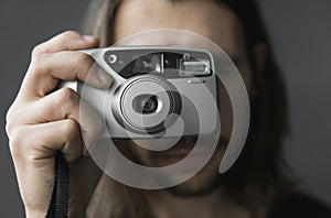 Handsome young bearded man with a long hair and in a black shirt holding vintage old-fashioned film camera on a black