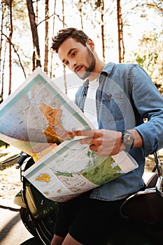 Handsome young bearded man near scooter looking at map