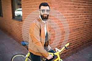 Handsome young bearded man while standing near his bicycle against the brick wall