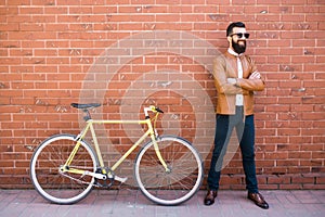 Handsome young bearded man while standing near his bicycle against the brick wall