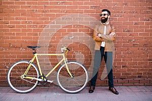 Handsome young bearded man while standing near his bicycle against the brick wall