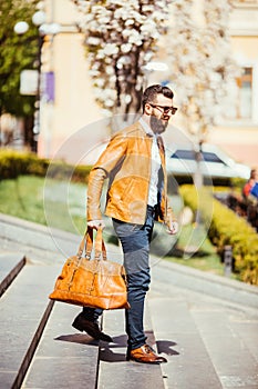 Handsome young bearded man in sunglasses walking down on the stairs with bag on city outdoors