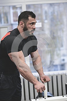 Handsome young bearded muscular man in black jersey rest relaxing in gym during hard workout training pause