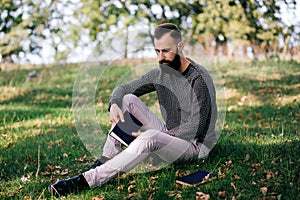 Handsome Young bearded student man hipster reading book in park on a summers sunny day