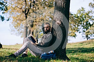 Handsome Young bearded student man hipster reading book in park on a summers sunny day