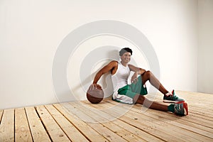 Handsome young black basketball player sitting on the wooden floor